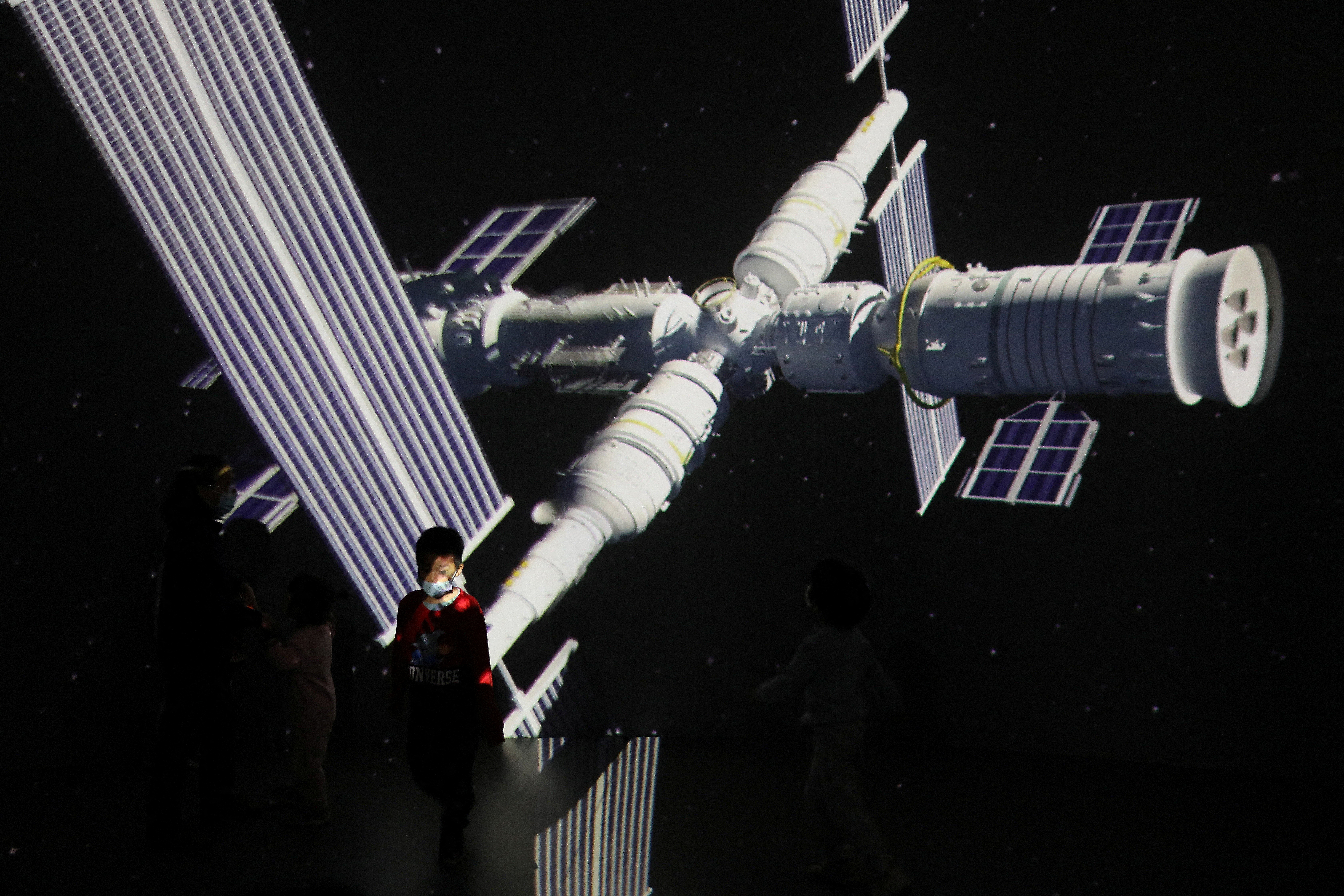 A child stands near a screen showing the image of the Tianhe space station