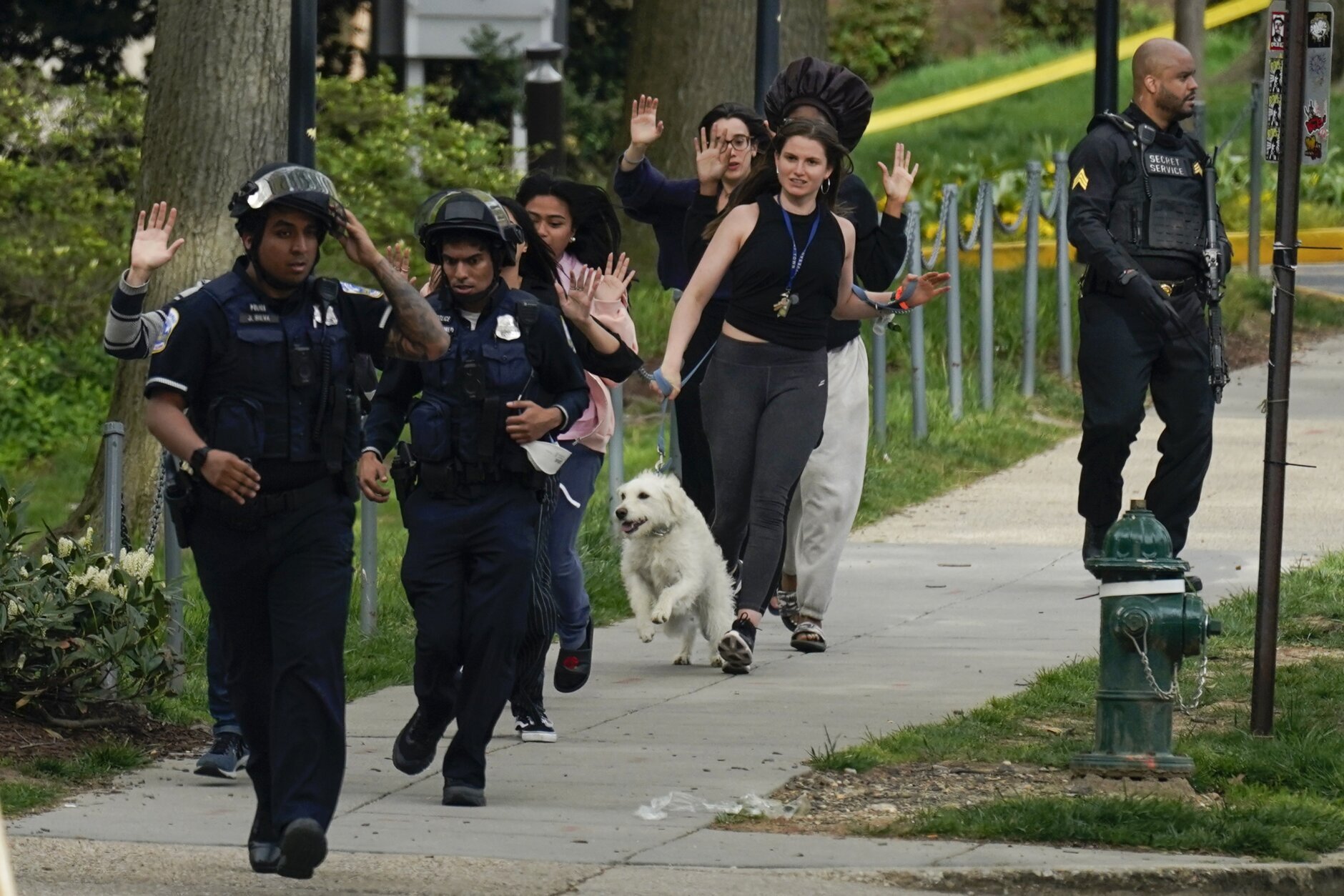 Police evacuate people, including Sarah Cope running with her dog, near the scene of a shooting Friday, April 22, 2022, in northwest Washington. Police say at least three people were injured in a shooting and city officials are warning people in the area to stay inside because of an "active threat." Dozens of law enforcement officers responded to the scene near Connecticut Avenue and Van Ness St. in the Van Ness neighborhood of Washington. (AP Photo/Carolyn Kaster)